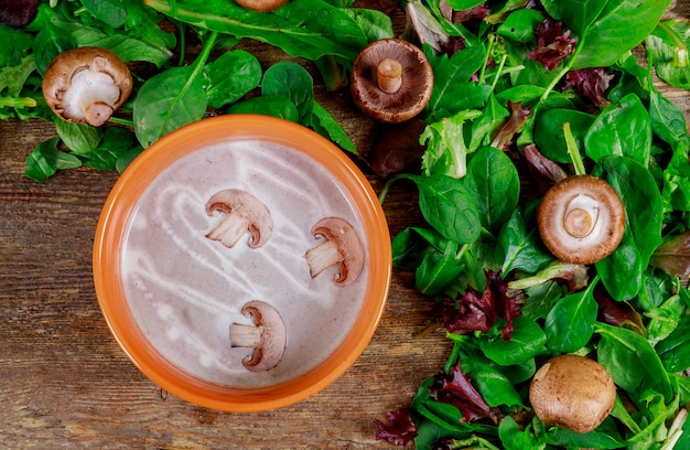 Velouté de champignons avec un bol violet sur une table en bois sombre.