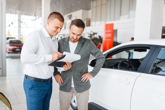 Le vendeur et l'acheteur font l'achat d'une nouvelle voiture dans la salle d'exposition. Client masculin achetant un véhicule en concession, vente d'automobiles