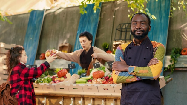 Vendeur afro-américain vendant des produits frais cultivés localement, présentant des fruits et légumes biologiques colorés. Jeune homme marchand de légumes ayant un marché de producteurs locaux, petite entreprise. Prise de vue à main levée.
