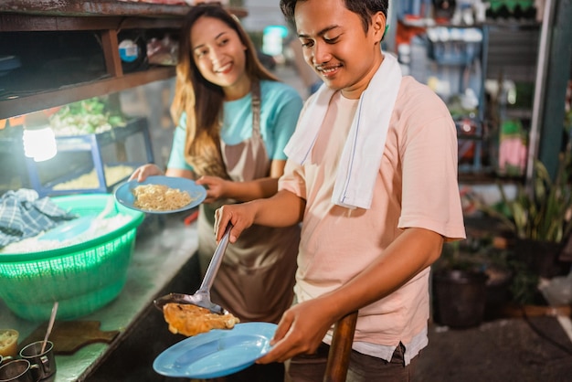 Vendeur asiatique mâle plaçant la main d'une femme sur un œuf au plat sur une assiette de nouilles