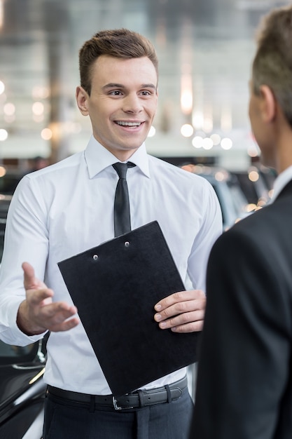 Vendeur et client. Beau jeune vendeur de voitures classiques parlant à un client et souriant