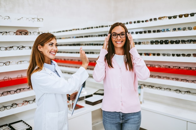 Vendeur et client de femmes d'âge moyen choisissant de nouvelles lunettes dans un magasin d'optique moderne. Notion de magasinage.