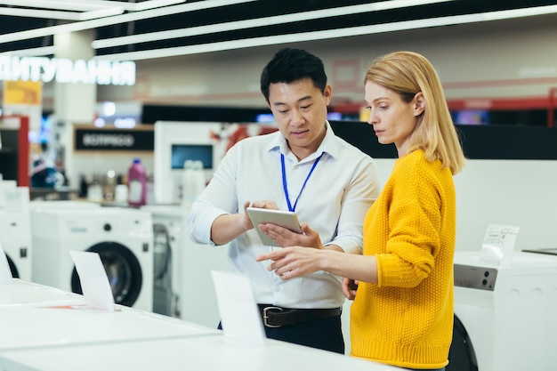 Vendeur consultant asiatique dans un magasin d'électronique et d'appareils électroménagers vendant une machine en état de marche à