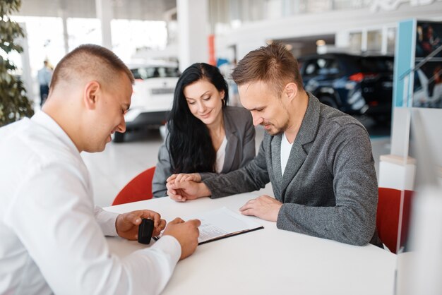 Un vendeur et un couple font la vente d'une nouvelle voiture dans la salle d'exposition.