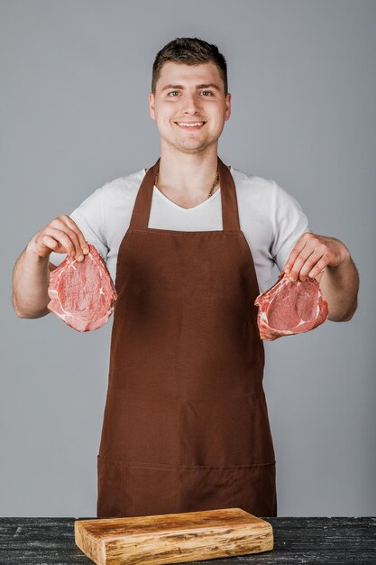 Un vendeur ou un cuisinier masculin tient de la viande crue dans ses mains et la montre sur un fond gris