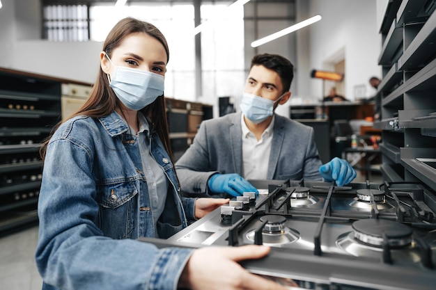 Un vendeur dans un hypermarché décrit les caractéristiques d'une cuisinière à gaz à une cliente portant des masques faciaux