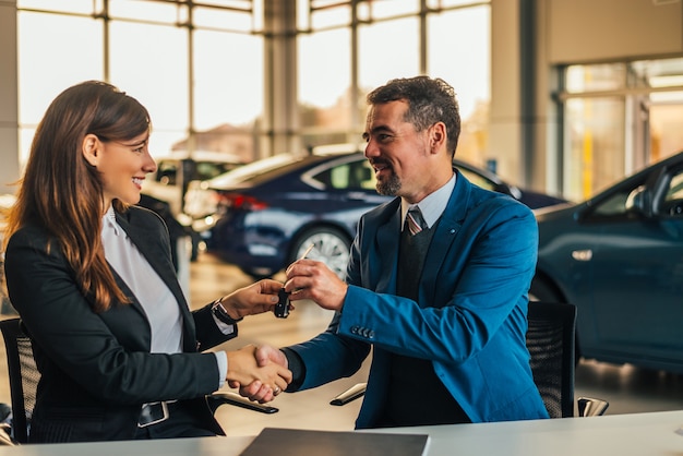 Vendeur donnant des clés de voiture en serrant la main d&#39;une femme dans un salon de l&#39;automobile.