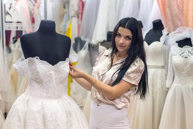 Vendeur de femme brune mesurant les détails de la robe de mariée