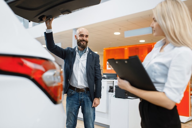 Photo vendeur d'homme et de femme à la recherche d'une voiture chez un concessionnaire automobile. cliente et vendeuse dans la salle d'exposition de véhicules, personne de sexe masculin achetant des transports, entreprise de concessionnaire automobile