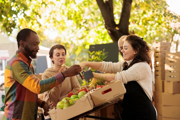 Vendeur offrant des échantillons aux clients tout en vendant des fruits et légumes cultivés sur place au marché de producteurs locaux. Jeune couple familial multiracial dégustant des produits biologiques naturels lors d'une visite à la foire alimentaire