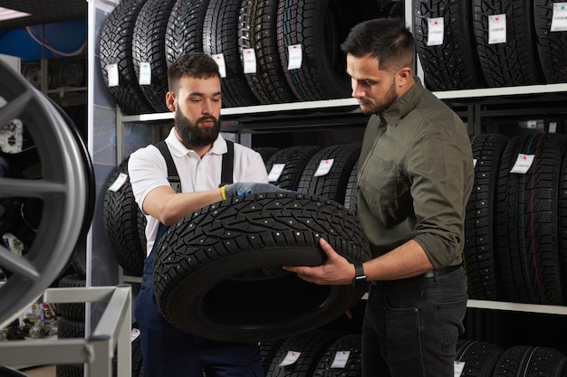 Un vendeur de pneus parlant de la caractéristique du produit au client est venu examiner l'assortiment représenté dans un atelier de service automobile