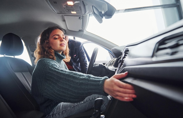 Vendeur professionnel aidant une jeune fille en choisissant une nouvelle automobile moderne à l'intérieur. Femme assise à l'intérieur.