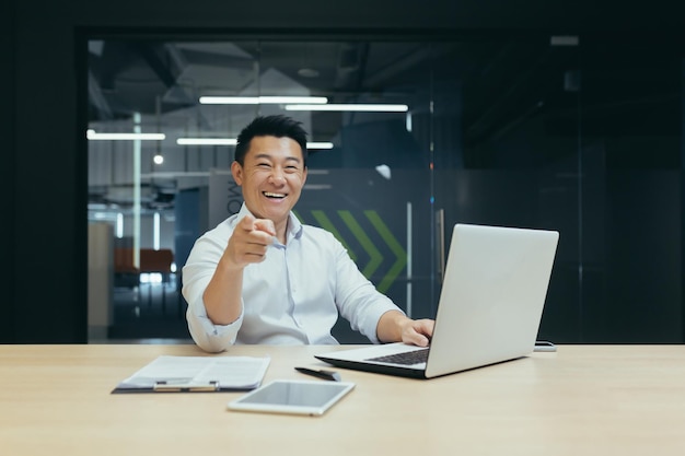 Vendeur prospère homme d'affaires asiatique heureux et souriant regardant la caméra pointant du doigt l'homme vers l'avant