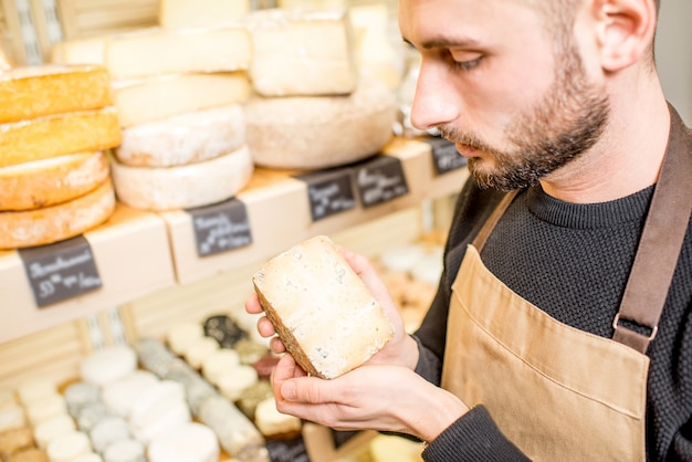 Vendeur tenant une paix de fromage bleu sur les étagères des magasins avec différents fromages