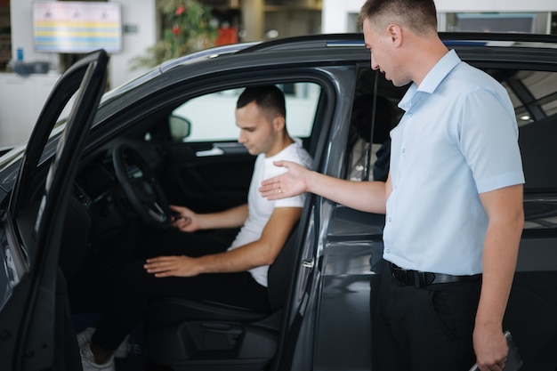 Vendeur vendant des voitures chez un concessionnaire automobile homme choisissant une voiture dans une salle d'exposition automobile