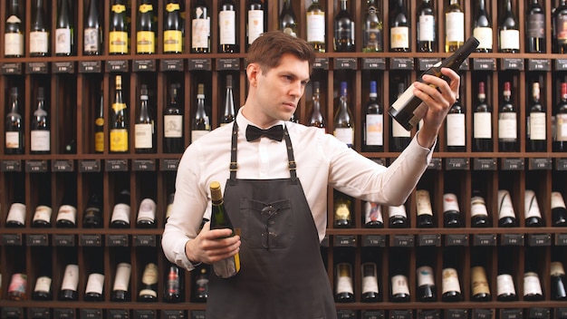 Vendeur de vin mignon détient des bouteilles de vin et lit l'étiquette dans un magasin de vin. Vous aide à choisir