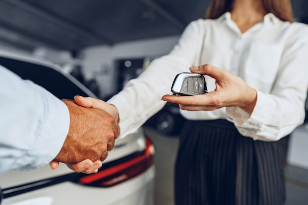 Vendeur de voiture et acheteur de poignée de main chez le concessionnaire automobile contre un nouveau fond de voiture