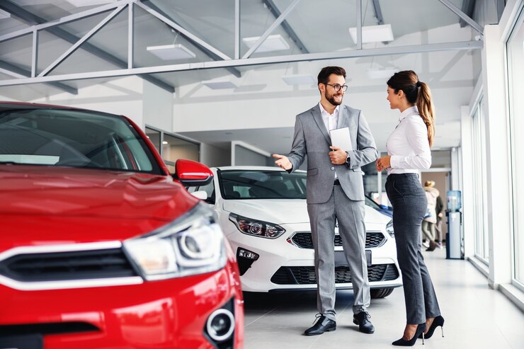 Vendeur de voiture souriant debout dans un salon de voiture avec le client et montrant autour des voitures en vente.