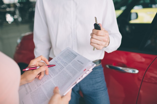 Vendeur de voiture sympathique parlant à une jeune femme et montrant une nouvelle voiture à l'intérieur de la salle d'exposition Signature du contrat.