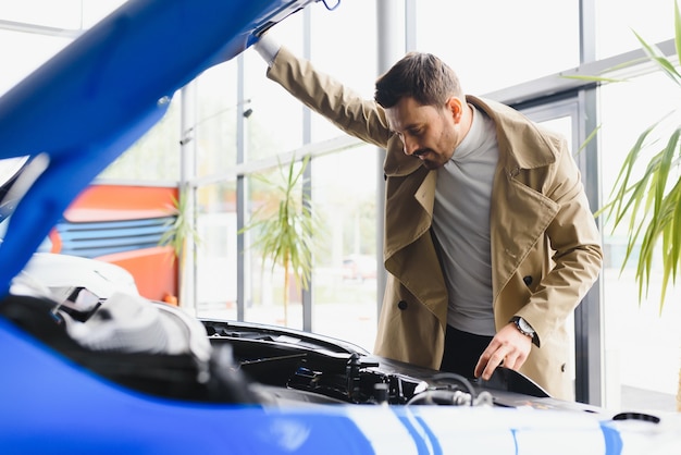 Vendeur de voitures d'âge moyen montrant le moteur au client chez le concessionnaire