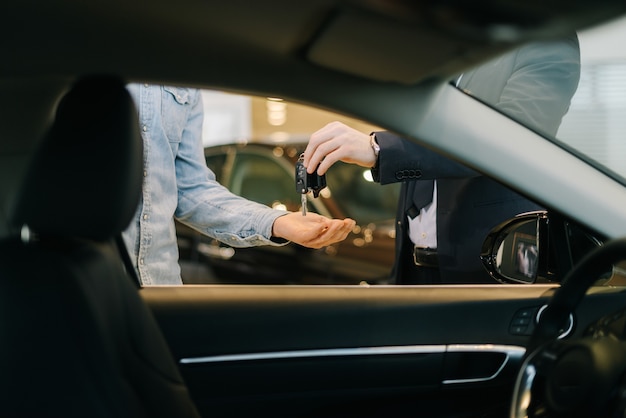 Photo vendeur de voitures remettant les clés d'une nouvelle voiture à un jeune acheteur chez un concessionnaire automobile