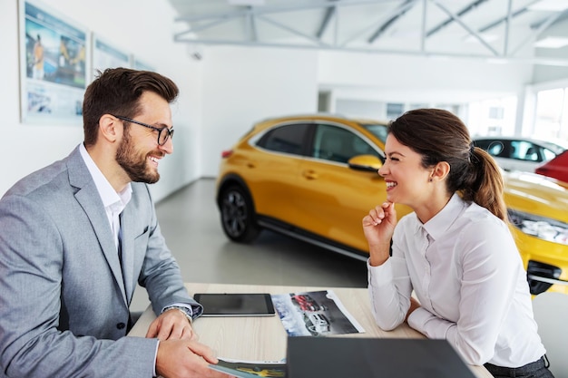 Vendeur de voitures sympathique souriant assis à la table avec un client et montrant une bonne offre au client