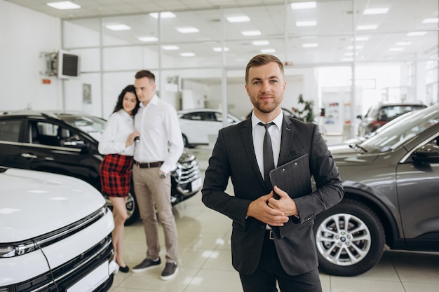 Des vendeurs de voitures amicaux souriants se tiennent dans le salon d'automobiles avec les bras croisés et annoncent la vente au détail
