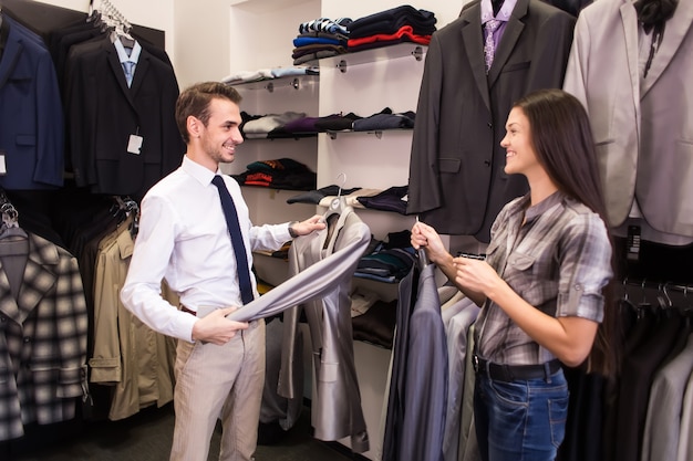 Une vendeuse aide à prendre un client dans une boutique de vêtements pour hommes