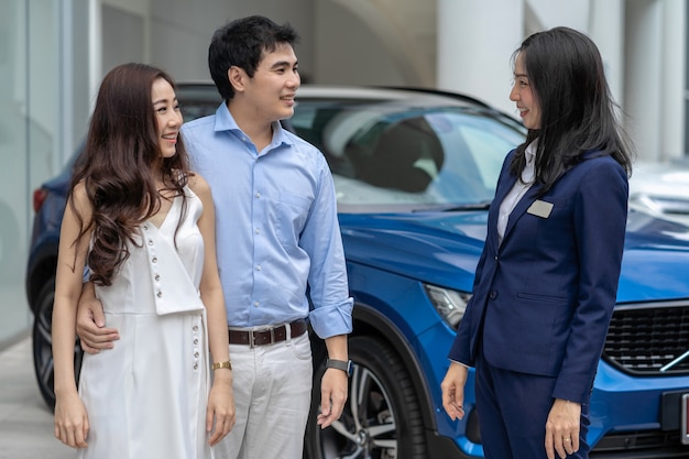 Vendeuse asiatique accueillant le couple client pour vérifier la voiture devant le showroom