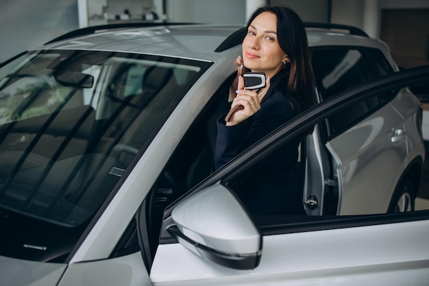 Une vendeuse dans une salle d'exposition de voitures tenant les clés de la voiture et debout à côté de la voiture