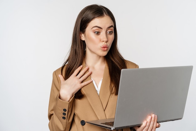 Vendeuse étonnée, femme d'affaires regardant un ordinateur portable avec un visage surpris et excité, debout sur fond blanc.