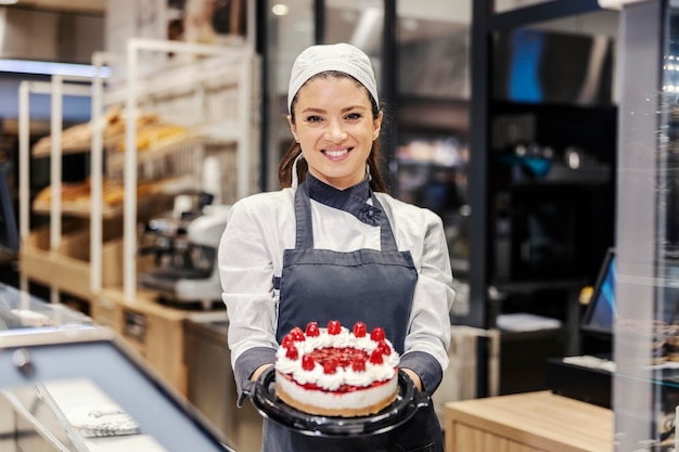 Une vendeuse heureuse dans le rayon boulangerie vendant un gâteau savoureux au supermarché