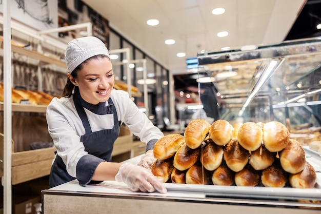 Une vendeuse heureuse mettant la pâtisserie prête à la vente au supermarché