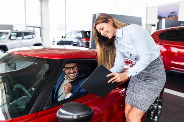 Photo vendeuse à la salle d'exposition de la concession parlant avec le client et l'aidant à choisir une nouvelle voiture pour lui-même.