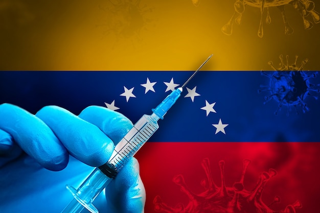 Venezuela Covid19 Campagne de vaccination La main dans un gant en caoutchouc bleu tient une seringue devant le drapeau