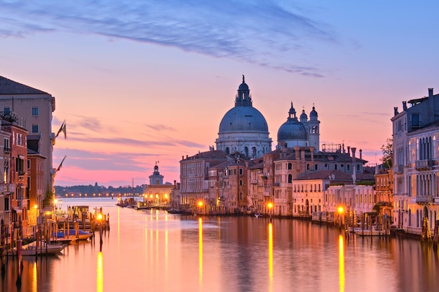 Venise romantique à l'aube, au lever du soleil. Image de paysage urbain du Grand Canal à Venise, avec la basilique Santa Maria della Salute reflétée dans la mer calme. Les lumières de la rue se reflètent dans l'eau calme.