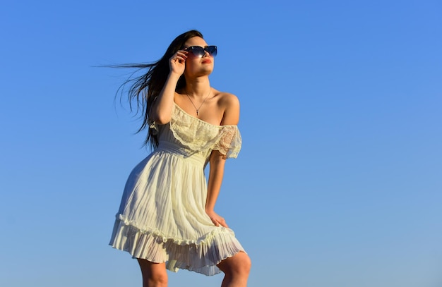 Vent du changement Modèle fantaisie en robe d'été tendre Vers l'été Liberté et harmonie Psychologie féminine Belle femme par temps ensoleillé ciel bleu Mode estivale Fille à lunettes de soleil copie espace