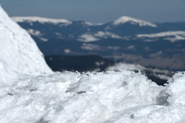 Le vent forme des grumeaux de glace sur le bord du précipice et la montagne hivernale derrière (pas au point)