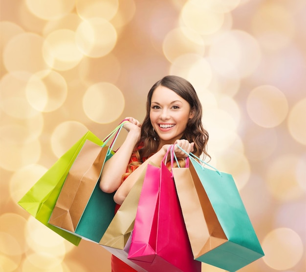 vente, cadeaux, noël, vacances et concept de personnes - femme souriante avec des sacs à provisions colorés sur fond de lumières beiges