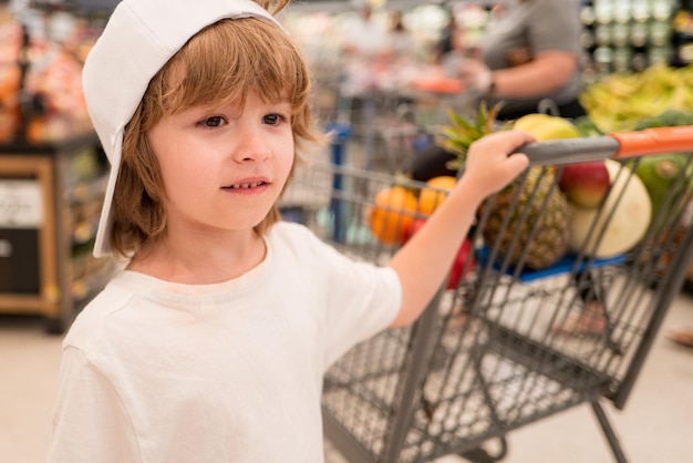 Vente consumérisme et concept de personnes heureux petit enfant avec de la nourriture dans le panier à l'épicerie