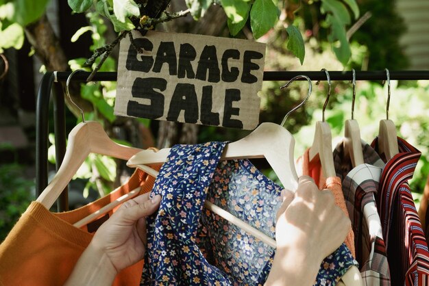 Vente de garage Mains féminines choisissant des vêtements usagés suspendus sur un rack