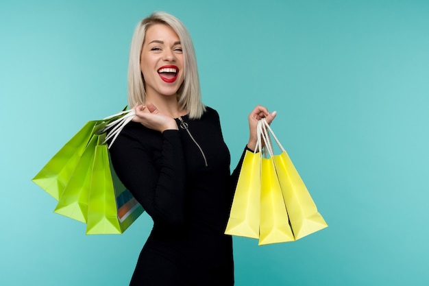 Vente. Jeune femme souriante tenant des sacs à provisions en vacances de vendredi noir. Fille heureuse sur fond bleu