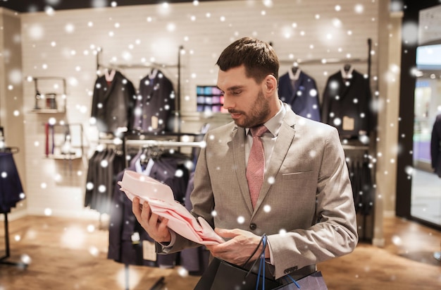 vente, mode, style et concept de personnes - jeune homme élégant ou homme d'affaires en costume avec des sacs d'achat choisissant une chemise dans un centre commercial ou un magasin de vêtements sur la neige