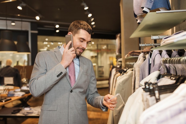 vente, shopping, mode, communication et concept de personnes - heureux jeune homme ou homme d'affaires appelant sur smartphone et choisissant des vêtements dans un magasin de vêtements