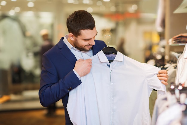 vente, shopping, mode, style et concept de personnes - élégant jeune homme en costume choisissant des vêtements dans un centre commercial ou un magasin de vêtements