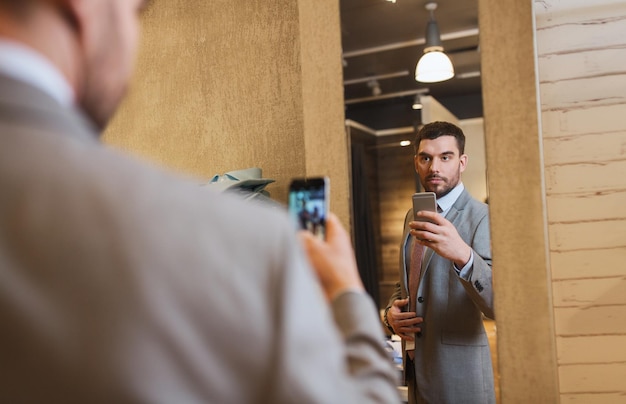 vente, shopping, mode, style et concept de personnes - jeune homme en costume avec smartphone prenant miroir selfie au magasin de vêtements