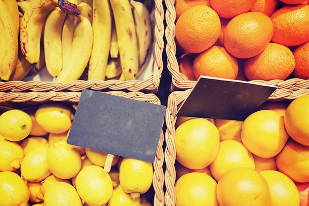 vente, shopping, vitamine c et concept d'alimentation écologique - fruits mûrs dans des paniers avec plaques signalétiques au marché de l'épicerie