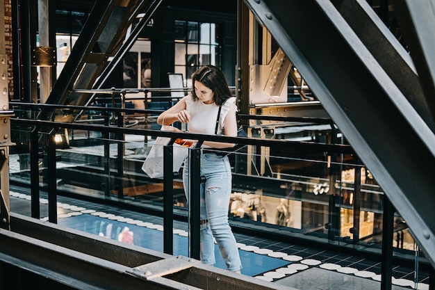 Vente vendredi noir jeune femme latina avec sacs à provisions et téléphone portable debout dans le shopping moderne