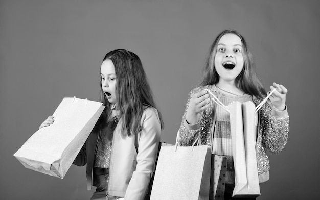 Ventes et remises Petites filles avec des sacs à provisions Fraternité et économies familiales sur les achats Enfants heureux Petite fille soeur Mode enfant Fond bleu grandes ventes journée de vente shopping vente