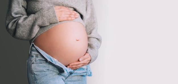 Ventre d'une belle femme enceinte en gros plan avec les mains dans des jeans déverrouillés Mère heureuse attendant la naissance du bébé Préparation à la maternité et concept d'attente